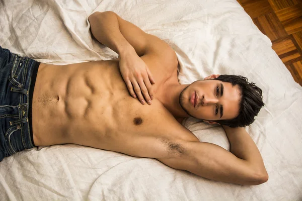 Tişörtsüz seksi erkek model yatağında tek başına yatıyor.