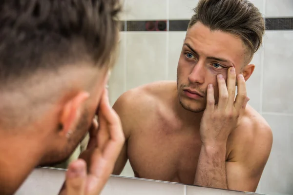 Young man touching his face while looking in mirror — Stok Foto