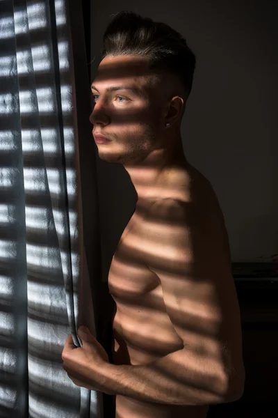 Pensiv topless man i skuggor ränder från fönstret — Stockfoto