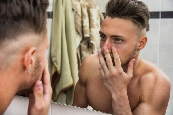 Young man touching his face while looking in mirror — Stok Foto