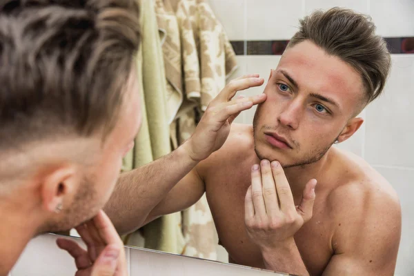 Young man touching his face while looking in mirror — Stock Photo, Image