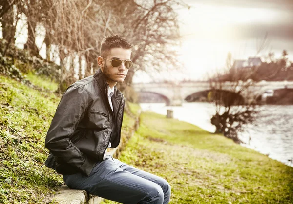 Στοχαστικός νεαρός άνδρας που κάθονται δίπλα σε ποτάμι — Φωτογραφία Αρχείου