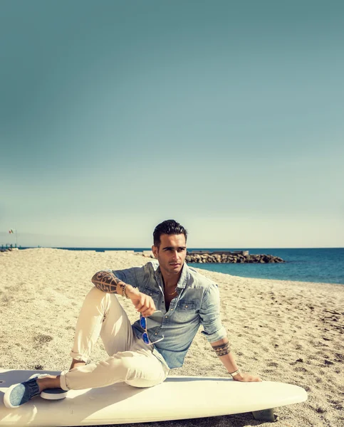 Uomo bello che si siede sul surf alla spiaggia — Foto Stock