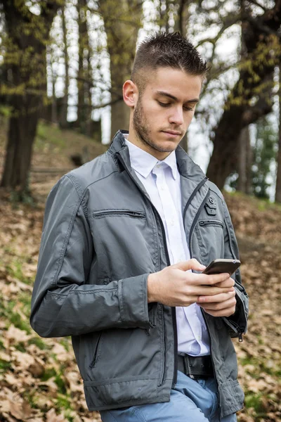 Mladý muž v parku pomocí mobilního telefonu — Stock fotografie