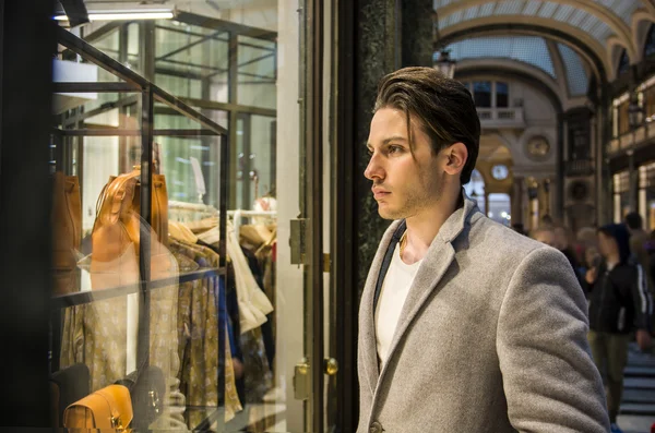 Hombre joven mirando artículos de moda en la ventana de la tienda — Foto de Stock