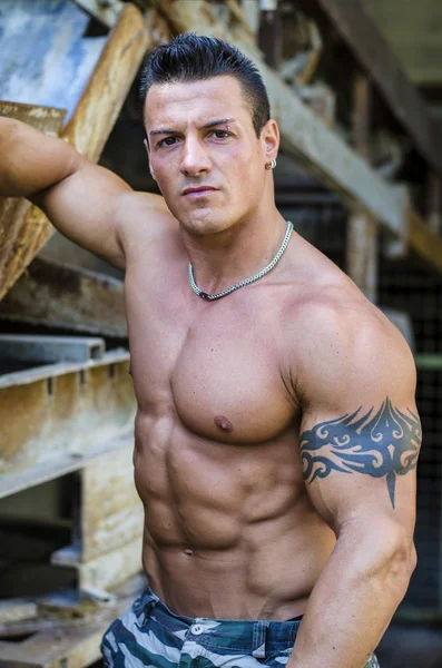 Handsome young muscle man with hand on rusty metal structure — Stock Photo, Image