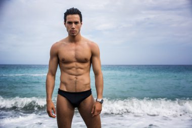 Okyanus kıyısında suda duran genç üstsüz atletik adam.