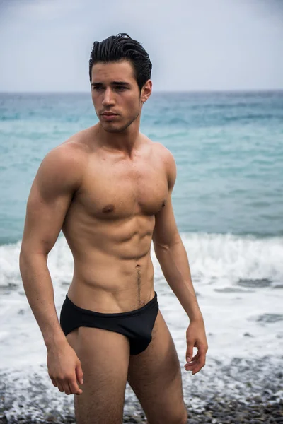 Young shirtless athletic man standing in water by ocean shore — Stock Photo, Image