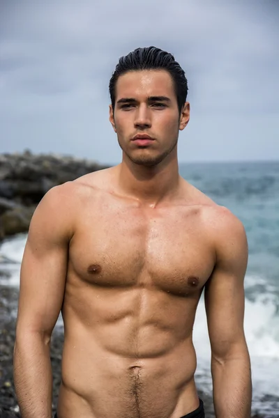 Okyanus kıyısında suda duran genç üstsüz atletik adam. — Stok fotoğraf