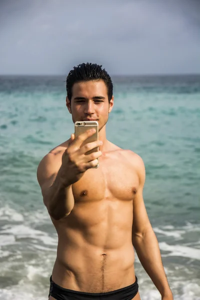 Üstsüz genç adam sahilde selfie çekiyor. — Stok fotoğraf