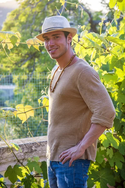 Zijaanzicht van de jongeman in hoed kijkend naar wijnbladeren — Stockfoto