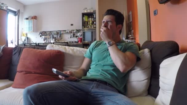 Jovem entediado sentado no sofá assistindo — Vídeo de Stock