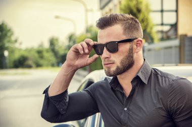 Handsome bearded man next to car in sunglasses