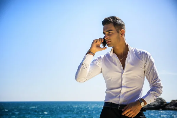 Young man at the seaside talking on cell phone — Stock Photo, Image