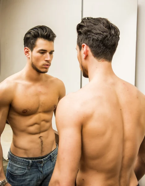Młody człowiek podziwiając swoje mięśnie w lustrze — Zdjęcie stockowe