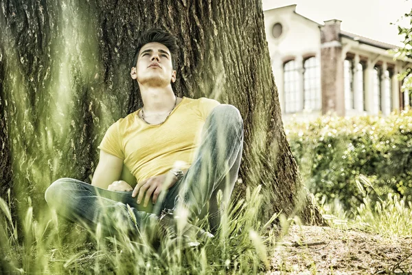 Jovem atraente no parque descansando contra a árvore — Fotografia de Stock