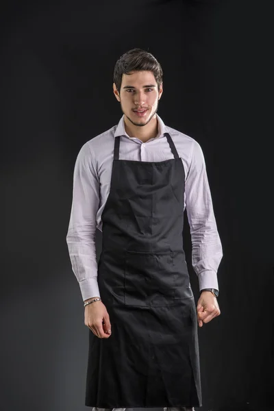 Jovem cozinheiro ou garçom, vestindo avental preto — Fotografia de Stock
