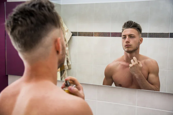 Handsome young man in bathroom, spraying cologne — Stock Photo, Image