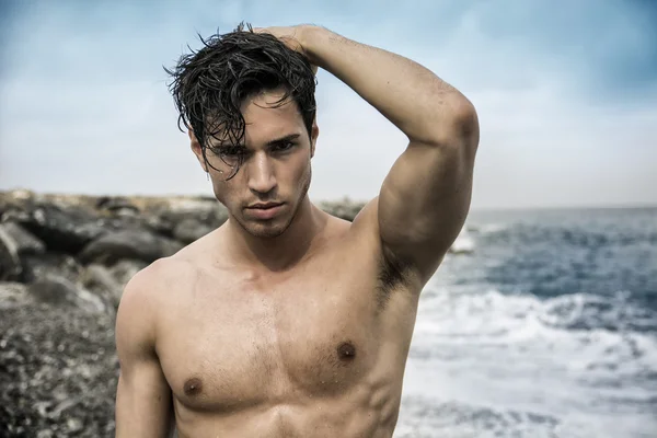 Young shirtless athletic man standing in water by ocean shore — Stock Photo, Image