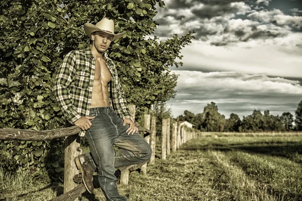 Retrato de hombre rústico sombrero con camisa desabrochada, apoyado en la valla de madera — Foto de Stock