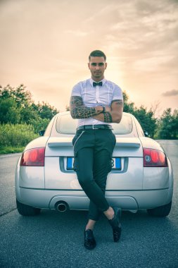 Beyaz gömlekli, arabanın yanındaki yakışıklı genç adam.