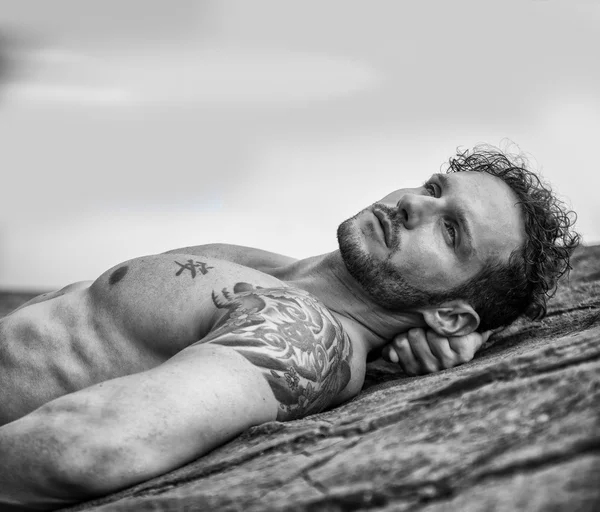 Bello muscoloso uomo sulla spiaggia sdraiato su rocce — Foto Stock