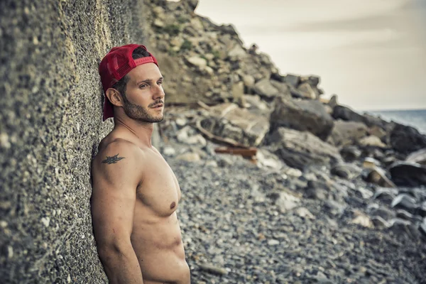 Uomo muscolare bello sulla spiaggia contro la roccia — Foto Stock