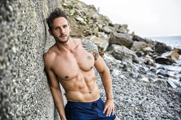 Hombre guapo musculoso en la playa contra roca —  Fotos de Stock