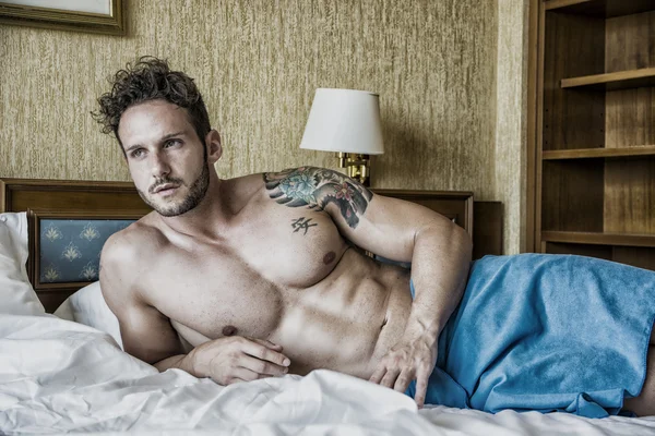 Shirtless sexy male model lying alone on his bed — Stock Photo, Image