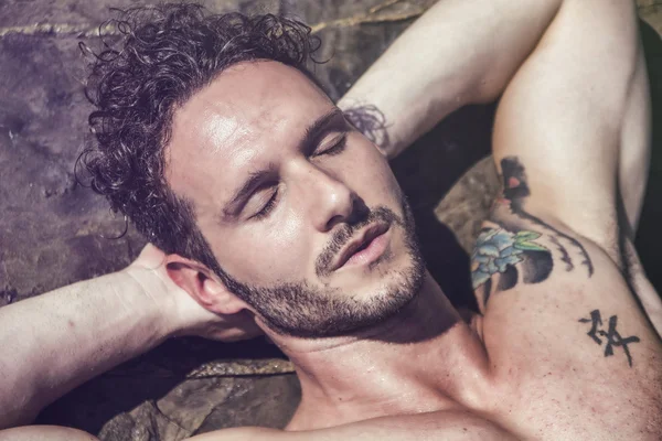 Handsome muscular man on the beach laying on rocks — Stock Photo, Image