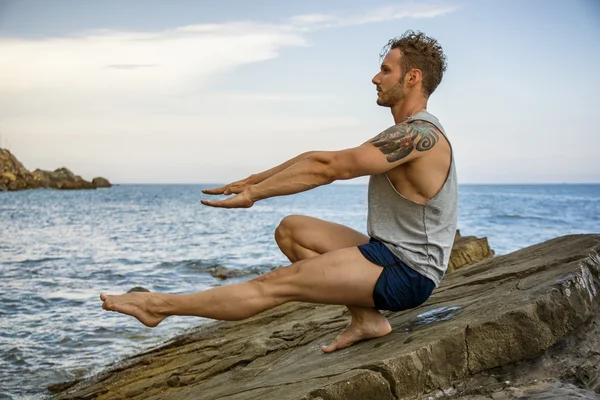 Athletic man exercising on rock by the sea — Stock Photo, Image