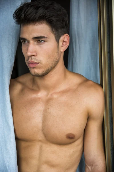 Sexy young man standing shirtless by curtains — Stock Photo, Image