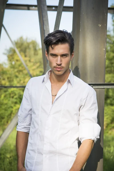 Handsome young man leaning against metal electricity trellis — Stock Photo, Image