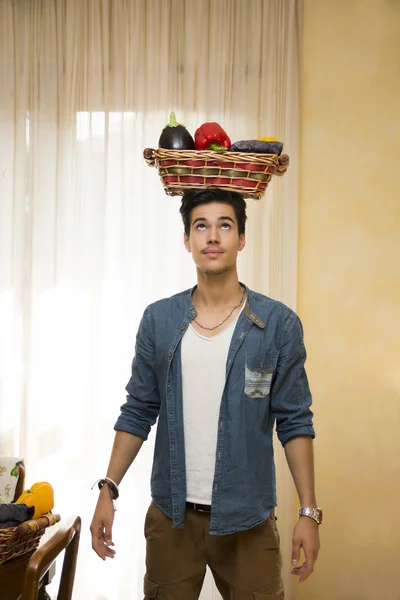 Jeune homme tenant un panier de légumes frais sur sa tête — Photo