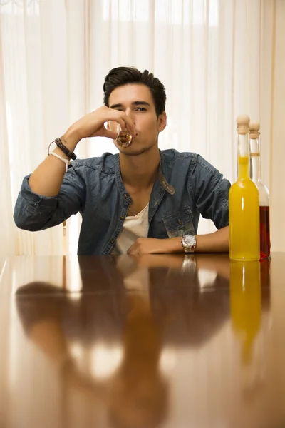 Joven sentado bebiendo solo en una mesa con dos botellas de licor — Foto de Stock