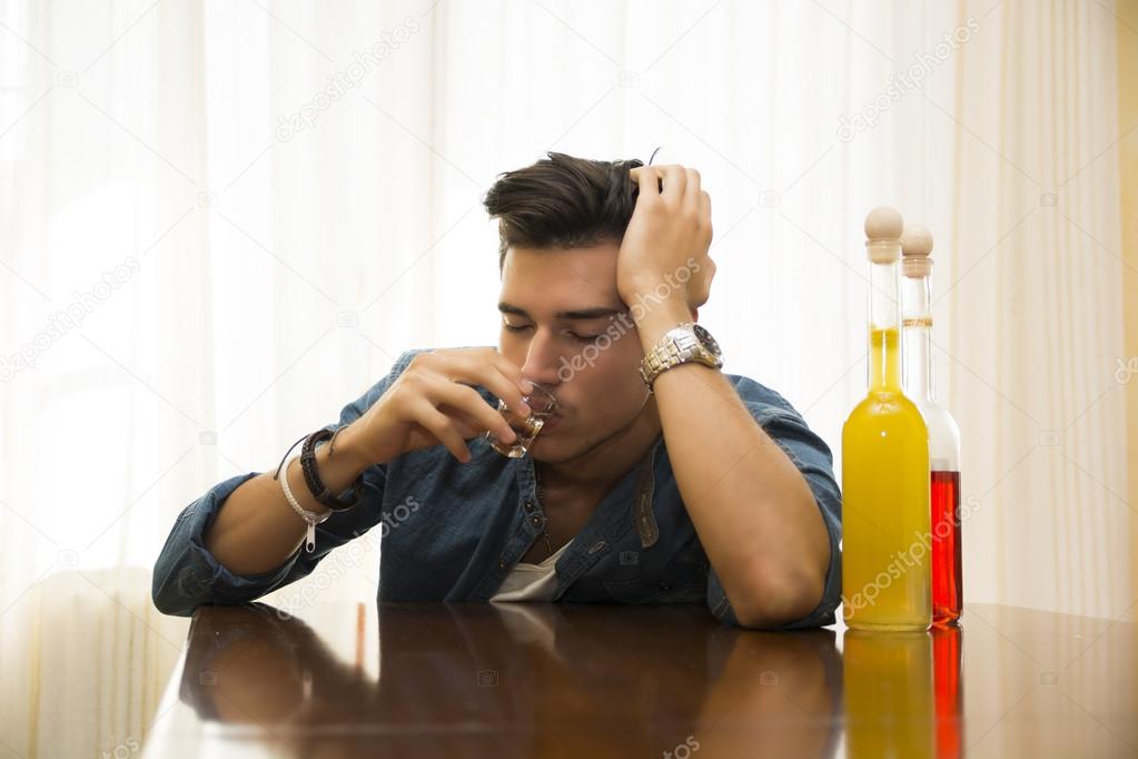 Sleepy, drunk young man sitting drinking alone at a table with two bottles