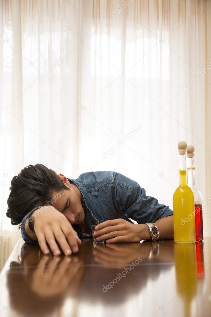 Young man drunk and sleeping alone at a table with two bottles of liquor