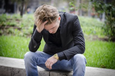 Depresyonda olan genç beyaz adam sokak kenarında oturuyor.
