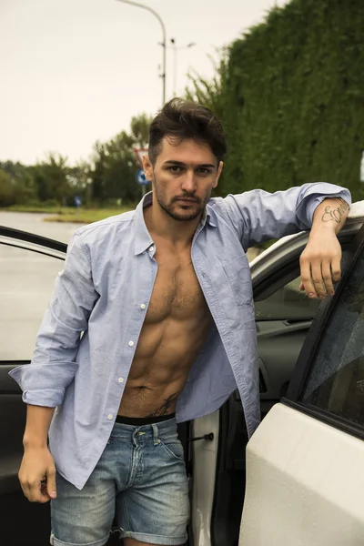 Przepiękny młody człowiek z koszula otwarte na nago mięśni tułowia zaczyna się jego samochód — Zdjęcie stockowe