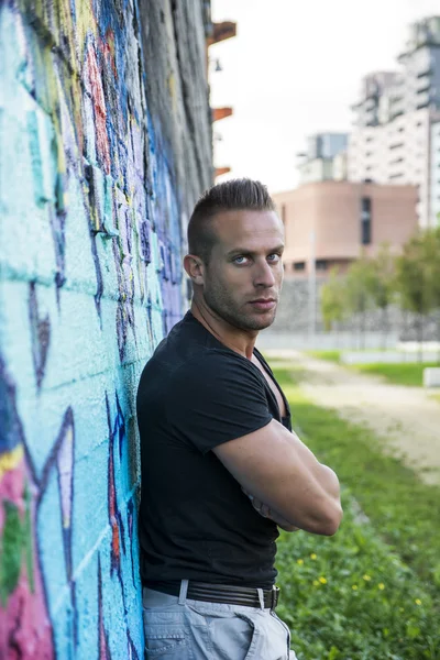Uomo muscolare bello che si appoggia contro il muro di graffiti variopinti — Foto Stock