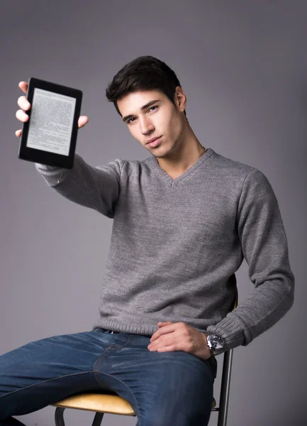 Hombre joven guapo sosteniendo y mostrando lector de ebook —  Fotos de Stock