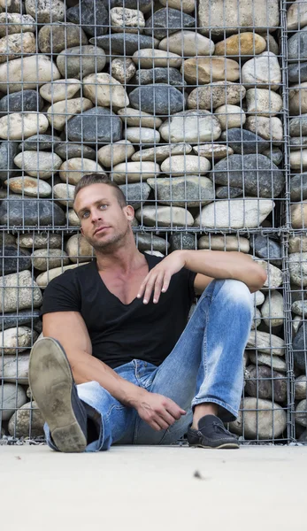 Uomo biondo muscoloso bello seduto contro il muro di pietre — Foto Stock