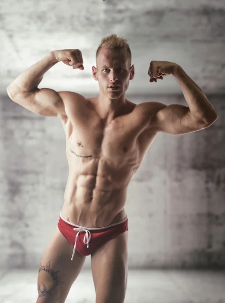 Knappe blonde gespierde shirtless jongeman doen biceps pose — Stockfoto