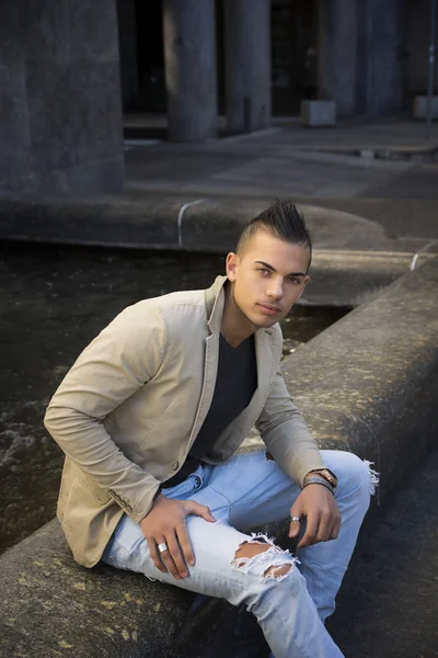 Aantrekkelijke jonge man in stedelijke omgeving, zittend op marmer — Stockfoto