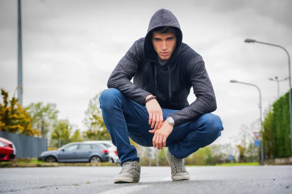 Attractive young man with hoodie and baseball cap in city street — Stock Photo, Image