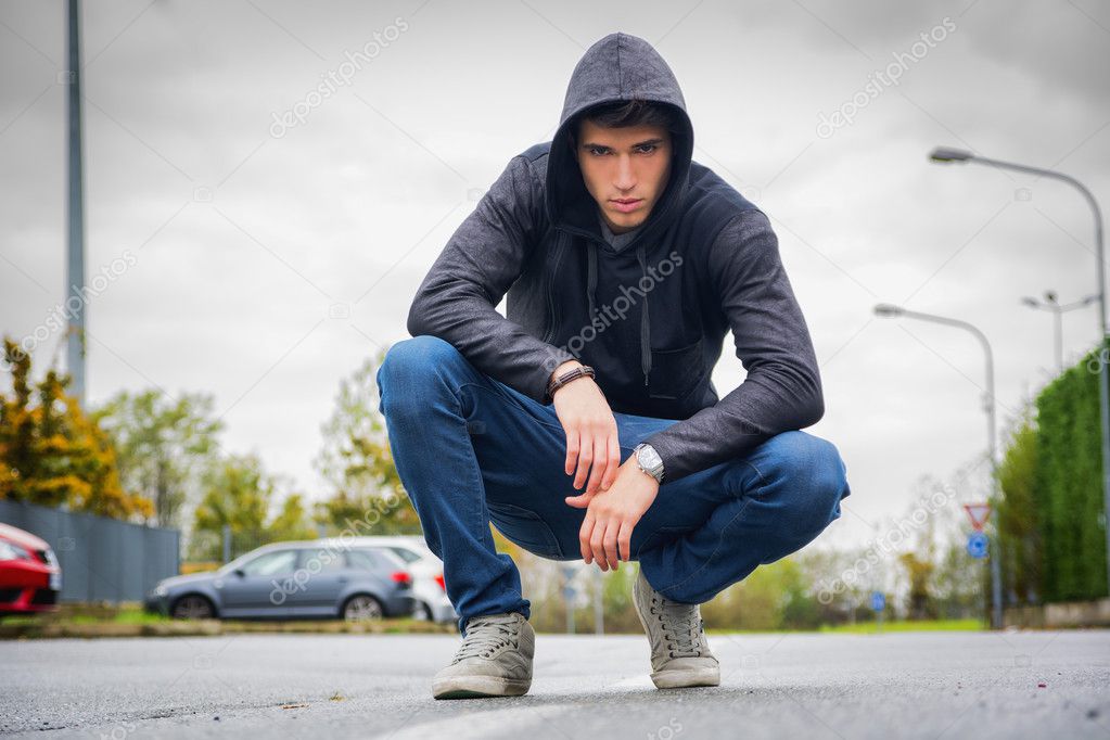 Attractive young man with hoodie and baseball cap in city street