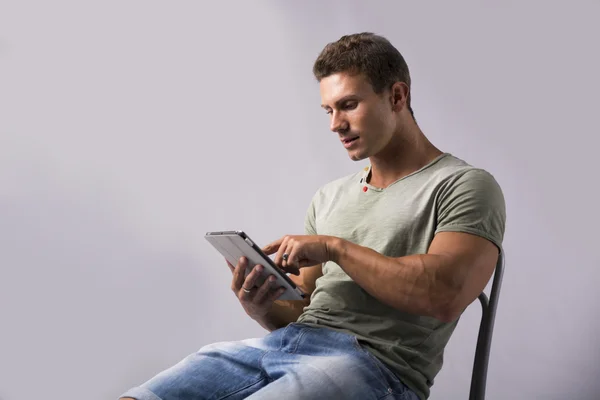 Gespierde jonge man zit op de stoel het lezen van e-boek apparaat — Stockfoto