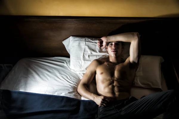 Knappe shirtless atletische jonge man in bed bij nacht — Stockfoto