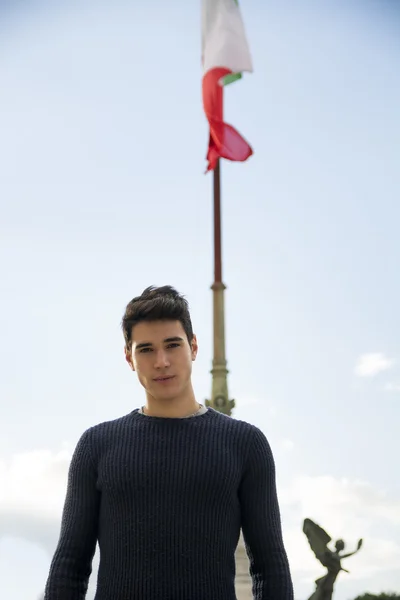 Красивый молодой человек перед итальянским флагом против синего неба — стоковое фото