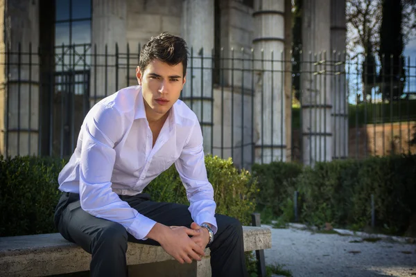 Przystojny młody mężczyzna w europejskie miasta, siedząc na ławce kamień — Zdjęcie stockowe